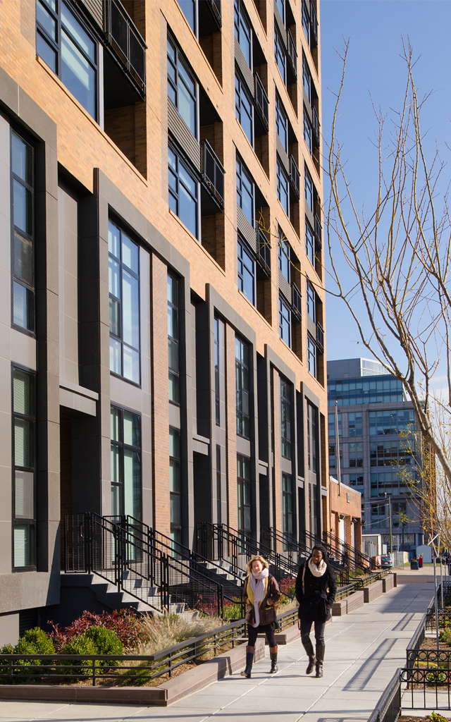 Rendering of tall building on busy city street with couple walking outside